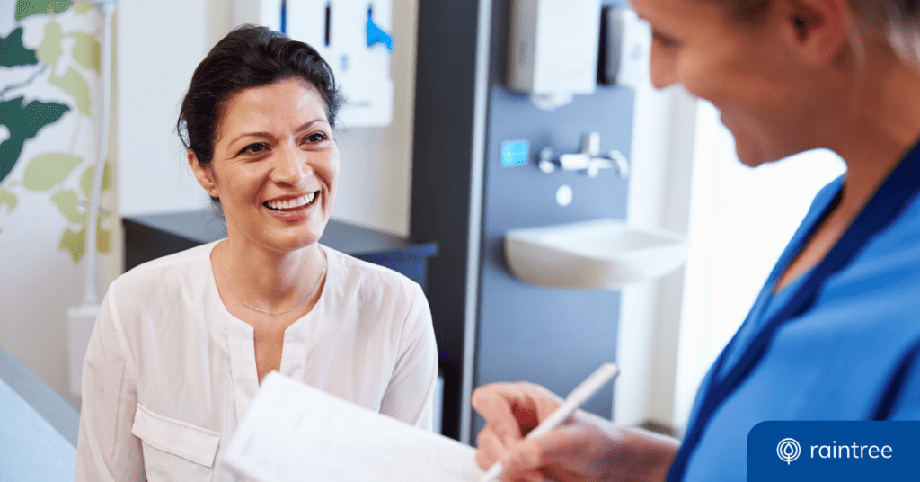 A Healthcare Provider Wearing Blue Scrubs Looks Down At A Patient, Who Smiles Back. Illustrating The Topic: &Quot;Improving Patient Payment Collection.&Quot;