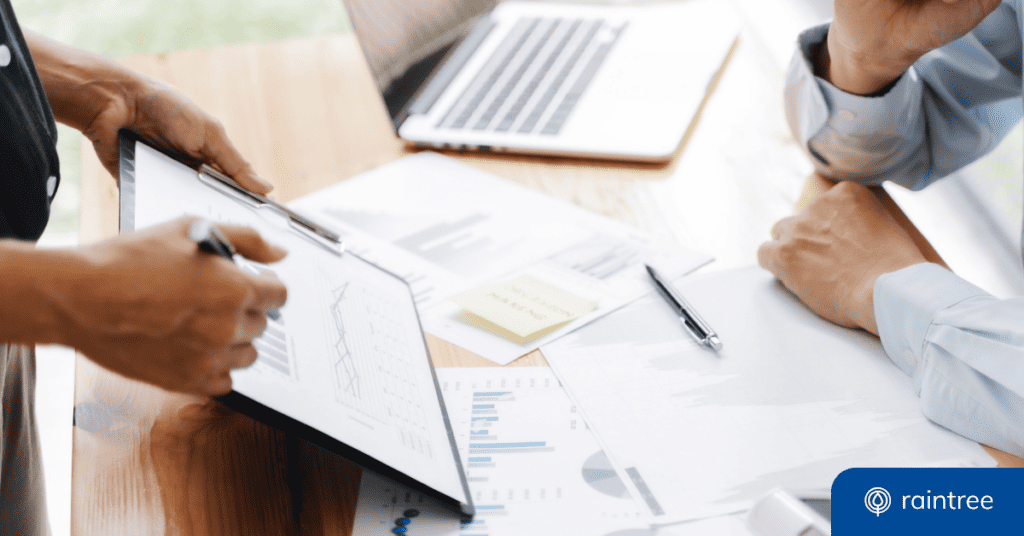 A close up of someone pointing to a chart on a clipboard, resting on another person's desk, which is covered in revenue metric charts. Illustrating the topic: "How to Boost Your RCM in Rehab Therapy."
