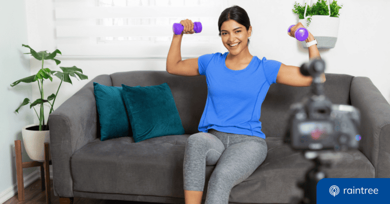 A person wearing exercise clothing sits on a gray couch holding two purple dumbbell weights, looking at a camera on a tripod and smiling. Illustrating the topic: "How to Grow Your Small Practice with Social Media."