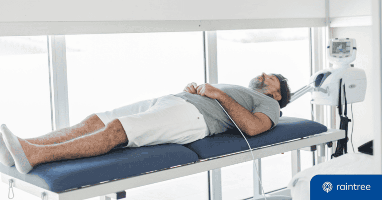 A man lies down on a table, connected to a machine. Illustrating the concept of "Tech in Physical and Occupational Therapy."