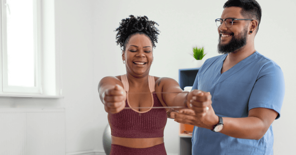 A physical therapist stands next to a patient, who wears a resistance band around her forearms, smiling. Illustrating the topic: "Building Better Clinical Workflows for Rehabilitation Therapy."
