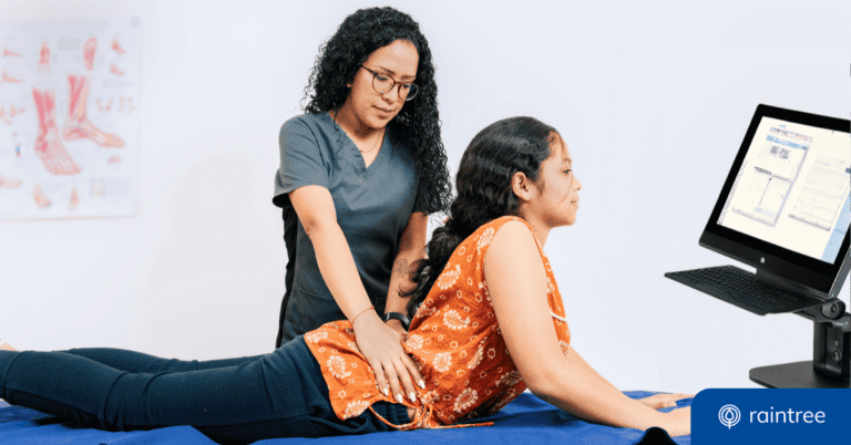 A physical therapist works with a young patient, with a desktop screen in the background and their electronic medical record software pulled up. Illustrating the concept of EMR Artificial Intelligence.
