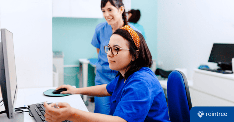 Two people wearing scrubs look at a computer screen, illustrating the topic: "EMR vs EHR: What's the difference?"