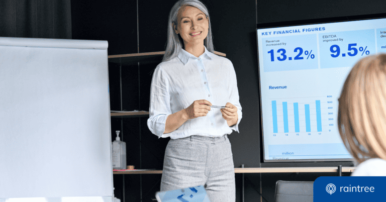 A physical therapy practice owner stands in front of a presentation screen, smiling at another person. The presentation shows key financial figures for business valuation, like revenue increase and EBITDA. Illustrating the topic: "When's the best time to sell your physical therapy practice?"