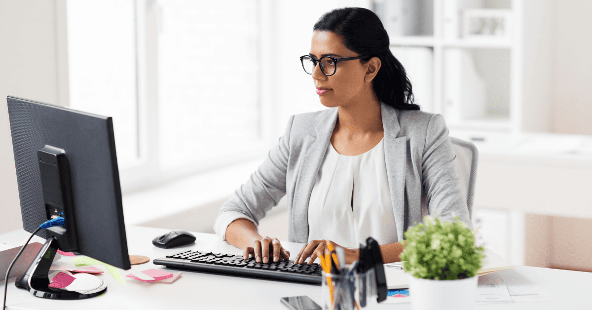 A Rehabilitation Therapy Practice Admin Looks At A Computer With A Thoughtful Expression, While Wearing Dark Glasses And A Gray Blazer. Illustrating The Topic: &Quot;Understanding Mips Hardship Exceptions For Physical Therapy, Occupational Therapy, And Speech Language Pathology&Quot;