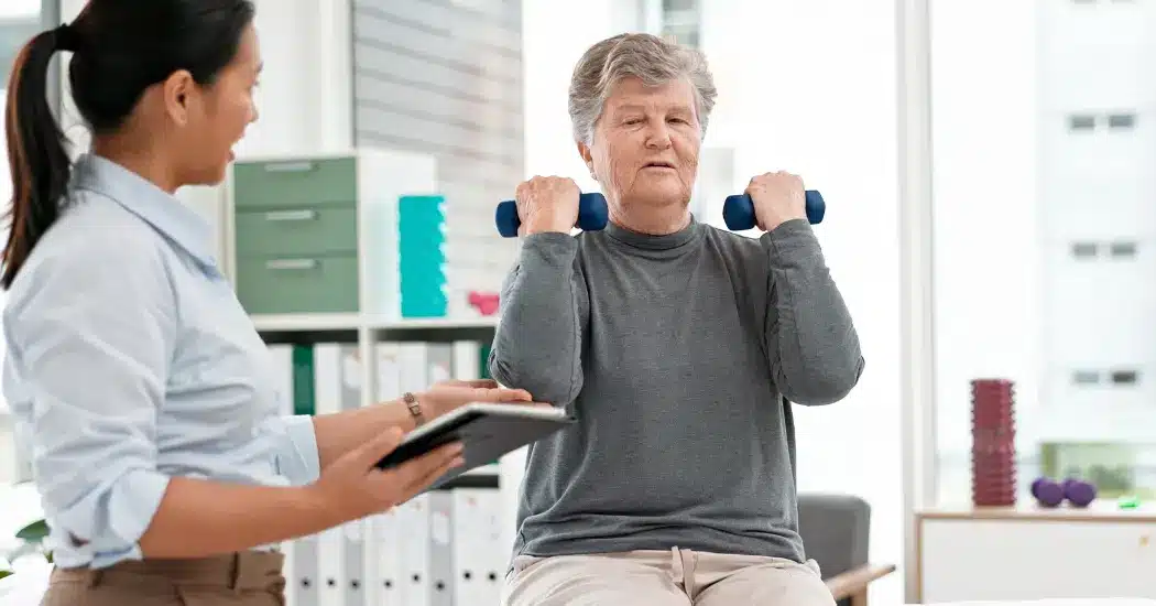 A physical therapist wearing a headset looks down at a computer monitor. Illustrating the topic: "What is Certified EHR Technology (CEHRT) and why is it important for rehab therapy?"