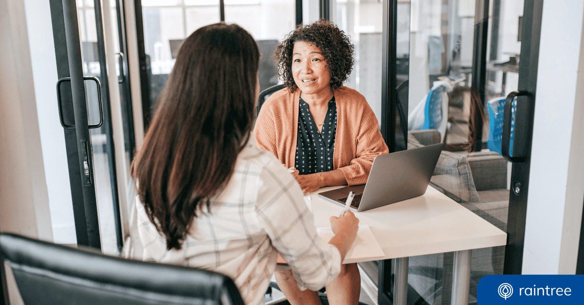 A human resources professional and a physical therapist sit at a desk, talking. Illustrating the topic: "Best Staff Retention Strategies for Rehab Therapy Clinics"