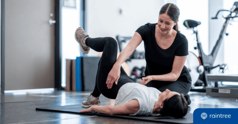 A physical therapist smiles at a patient, who is laying on a yoga mat with one leg elevated in the air. Illustrating the topic: "How to Improve Patient Satisfaction in Physical Therapy Practices Using Business Intelligence Tools and Patient Data"