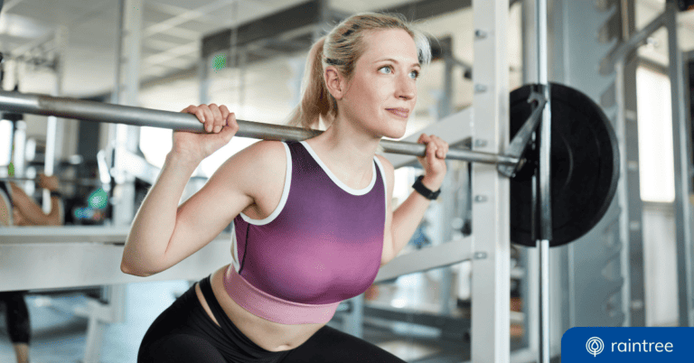 A blonde physical therapy patient wearing a sports bra and high-waisted leggings squats with a barbell on her shoulders, looking straight ahead. Illustrating the topic: "Patient Journey Map Ways to Ace the PT Patient Experience"