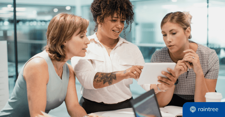 Three professionals gather over a desk to perform a HIPAA security risk assessment. The person in the middle speaks while holds a tablet, and the other two look on with calm expressions.