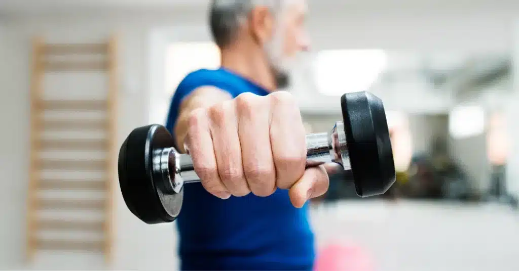 A physical therapy Medicare patient wearing a blue shirt holds up a single dumbbell. Illustrating the topic, "What is the Medicare 8-minute rule?"