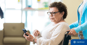 A Medicare patient looks at her phone while a physical therapist pushes her wheelchair. She has a concerned expression. Illustrating the topic of billing mistakes and the importance of claim scrubbing.
