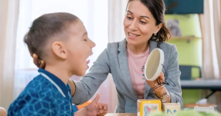 A Speech Therapist Works With A Preschool Aged Boy, Who Is Sticking His Tongue Upward And Looking Into A Mirror. Illustrating The Topic Of Speech Therapy Cpt Codes.