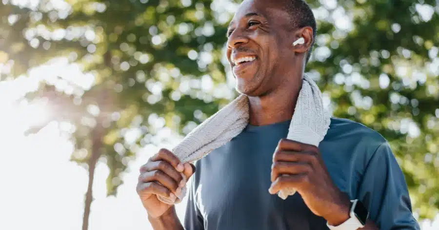 A gait training physical therapy patient smiles while listening to earbuds and wearing a smartwatch during an outdoor walk. Illustrating the importance of CPT code 97116.