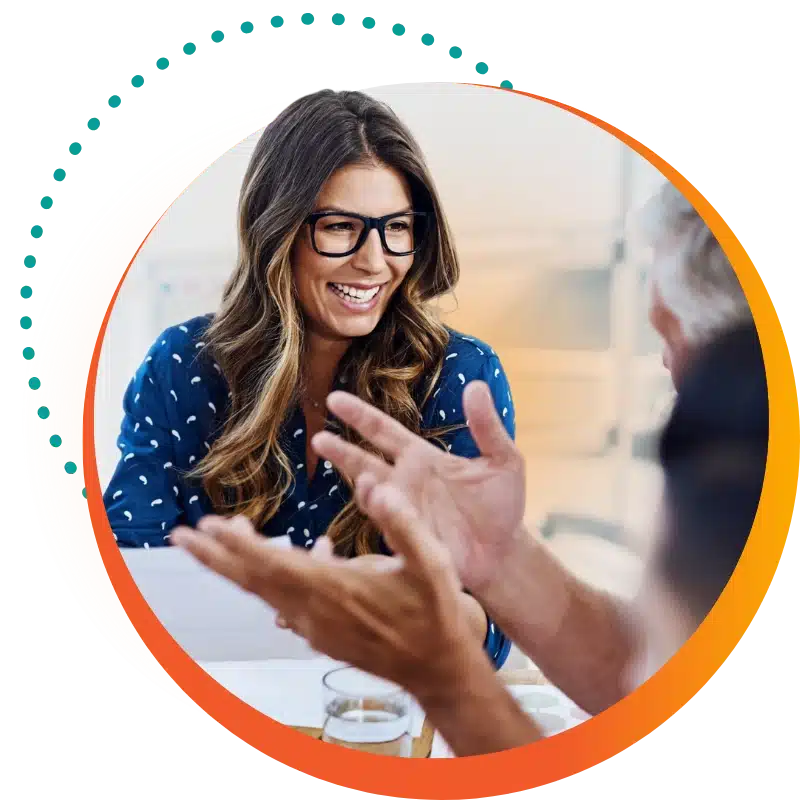 Raintree Careers Header: A Woman With Long Hair And A Dark Blue Shirt Smiles At A Colleague During A Group Meeting.