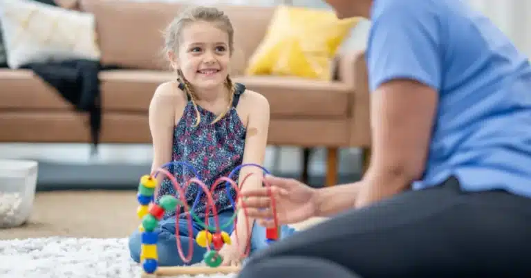 A Young Child Looks Up At A Bcba During An Applied Behavior Analysis Session, Illustrating The Topic Of Reducing Turnover In Aba Therapy.