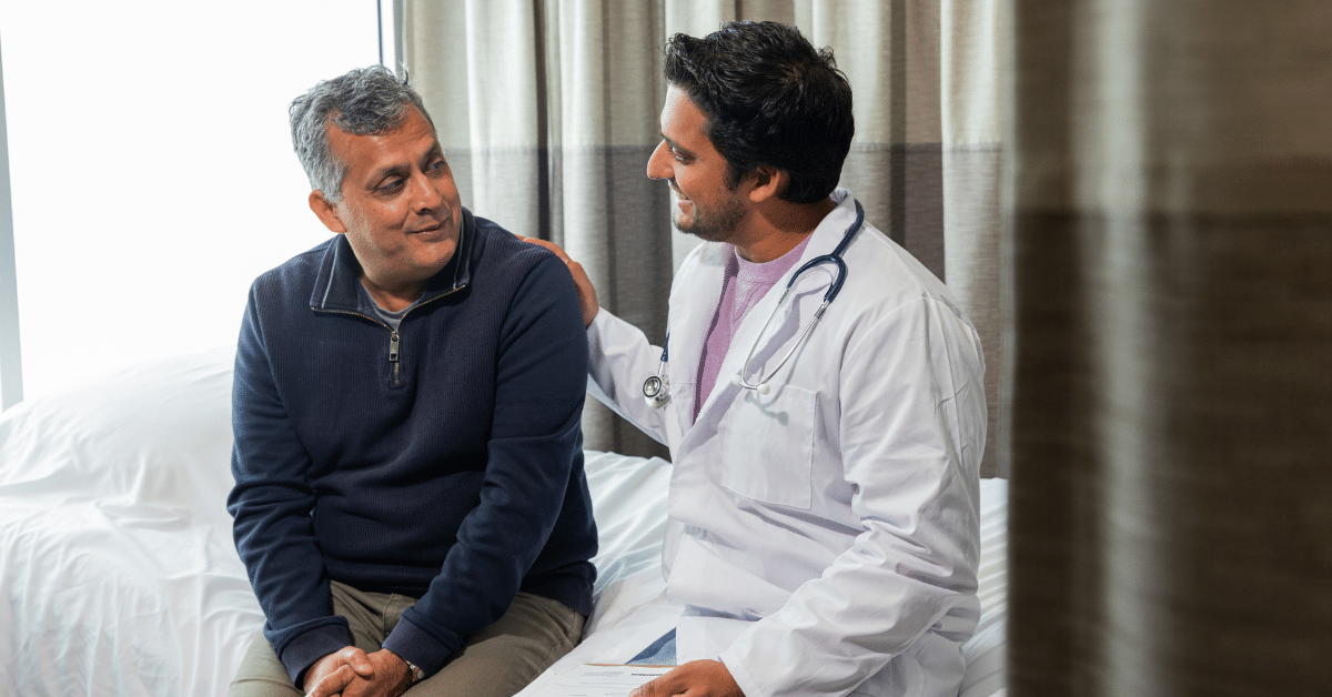 A physician smiles and touches the shoulder of a surgical patient, illustrating the topic of referral management in rehab therapy.